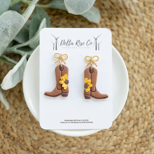 Handmade polymer clay earrings featuring western cowgirl boots accented with bright sunflower details. These lightweight statement earrings combine rustic country charm with floral western style for a fun and wearable accessory. Designed for comfortable all-day wear, they are perfect for rodeos, country concerts, fairs, festivals, western-themed events, or everyday outfits. The sunflower detail adds a cheerful touch that pairs beautifully with denim, boots, dresses, and casual country fashion. A unique hand