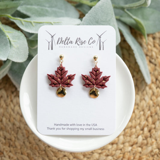 Handmade maroon autumn leaf earrings with gold accents and charm details, perfect for fall and Thanksgiving. These lightweight polymer clay earrings feature deep maroon leaves paired with elegant golden highlights, creating a stylish seasonal accessory. Designed for comfort and durability, they’re an ideal choice for fall fashion, autumn celebrations, or gifting to someone who loves unique handmade jewelry.
