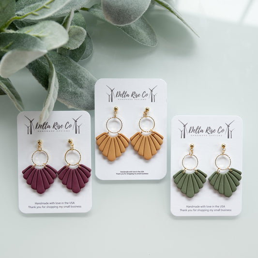 Handmade fan-style earrings in fall colors including plum, green, and mustard, perfect for autumn fashion. Lightweight polymer clay earrings feature layered fan shapes that add movement and seasonal style, making them ideal for Thanksgiving, fall festivals, cozy autumn outfits, or gifting to lovers of handmade jewelry. Statement dangle earrings designed for comfort and unique seasonal flair.