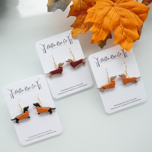 Handmade dachshund earrings wearing cozy sweaters, perfect for dog lovers and autumn/winter fashion. Lightweight polymer clay earrings feature cute pups in colorful knit sweaters, adding whimsical charm to seasonal outfits, casual wear, or gifting. Unique handmade jewelry for pet enthusiasts, combining playful design, comfort, and festive autumn or winter style for statement accessory lovers.